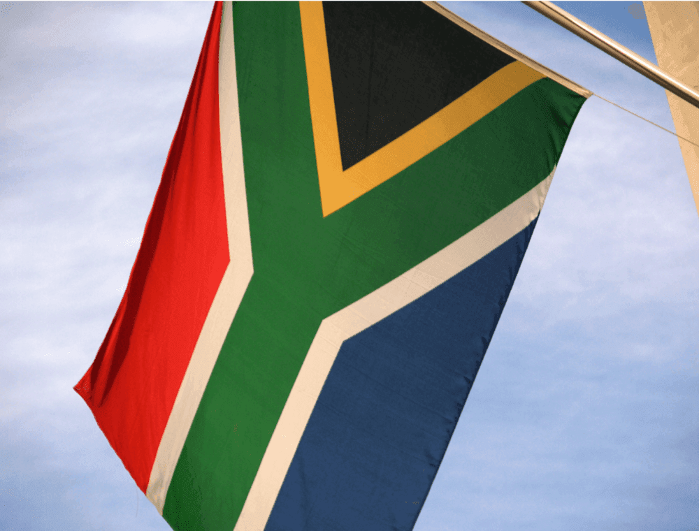 The South African flag flies against a blue sky. The flag features six colors: black, yellow, green, white, red, and blue. - Home Instead
