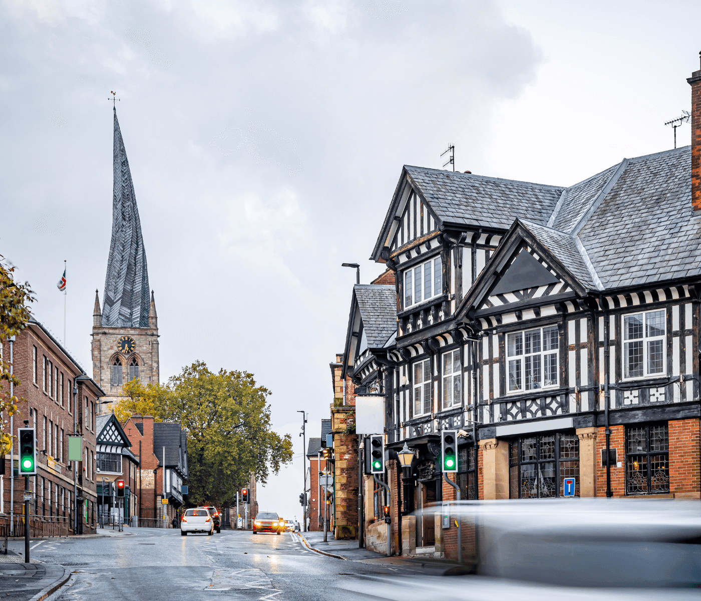 Street view of a town with old half-timbered buildings and a tall, pointed church steeple in the background. - Home Instead