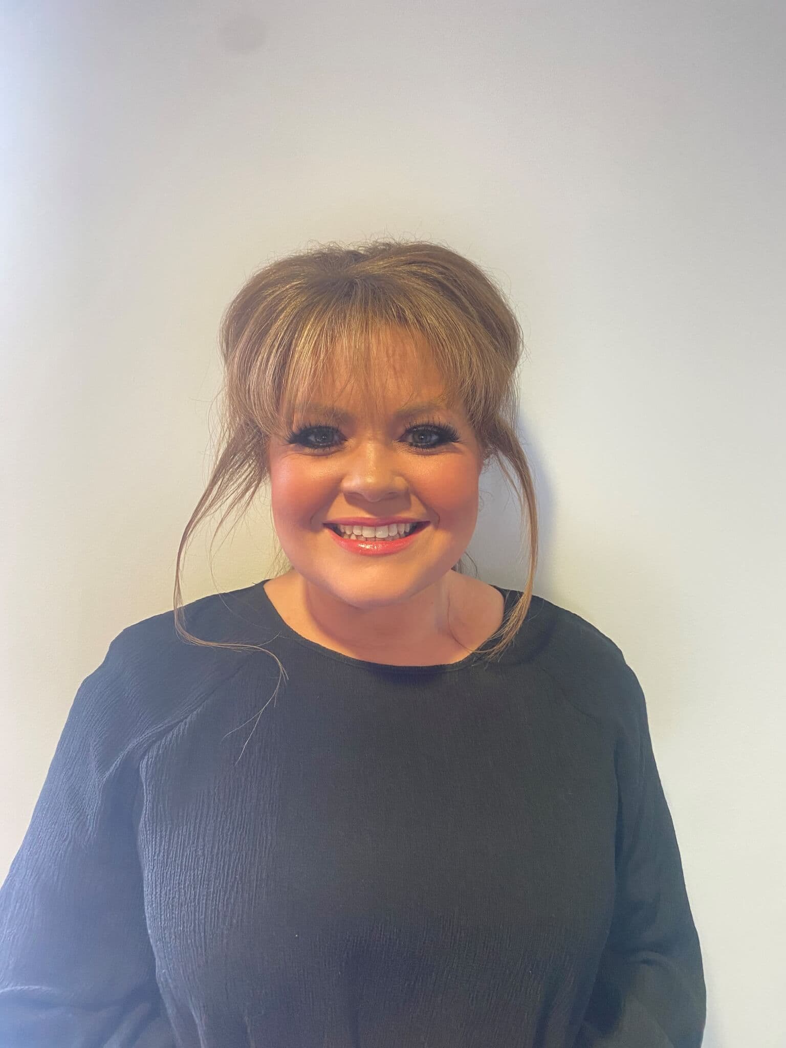 Woman with brown hair in an updo, wearing a black top, smiling against a plain white background. - Home Instead