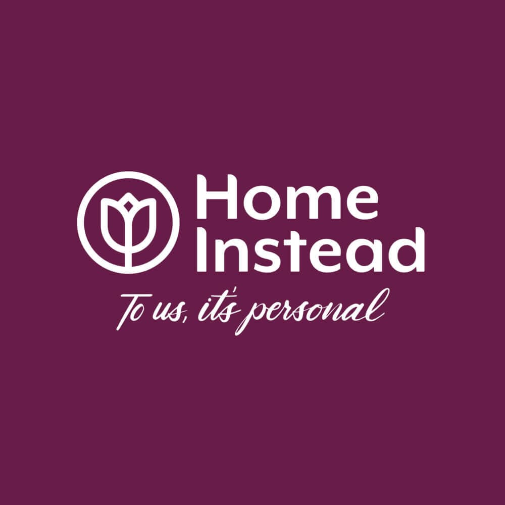Home Instead logo with a flower icon and the tagline "To us, it's personal" on a purple background. - Home Instead