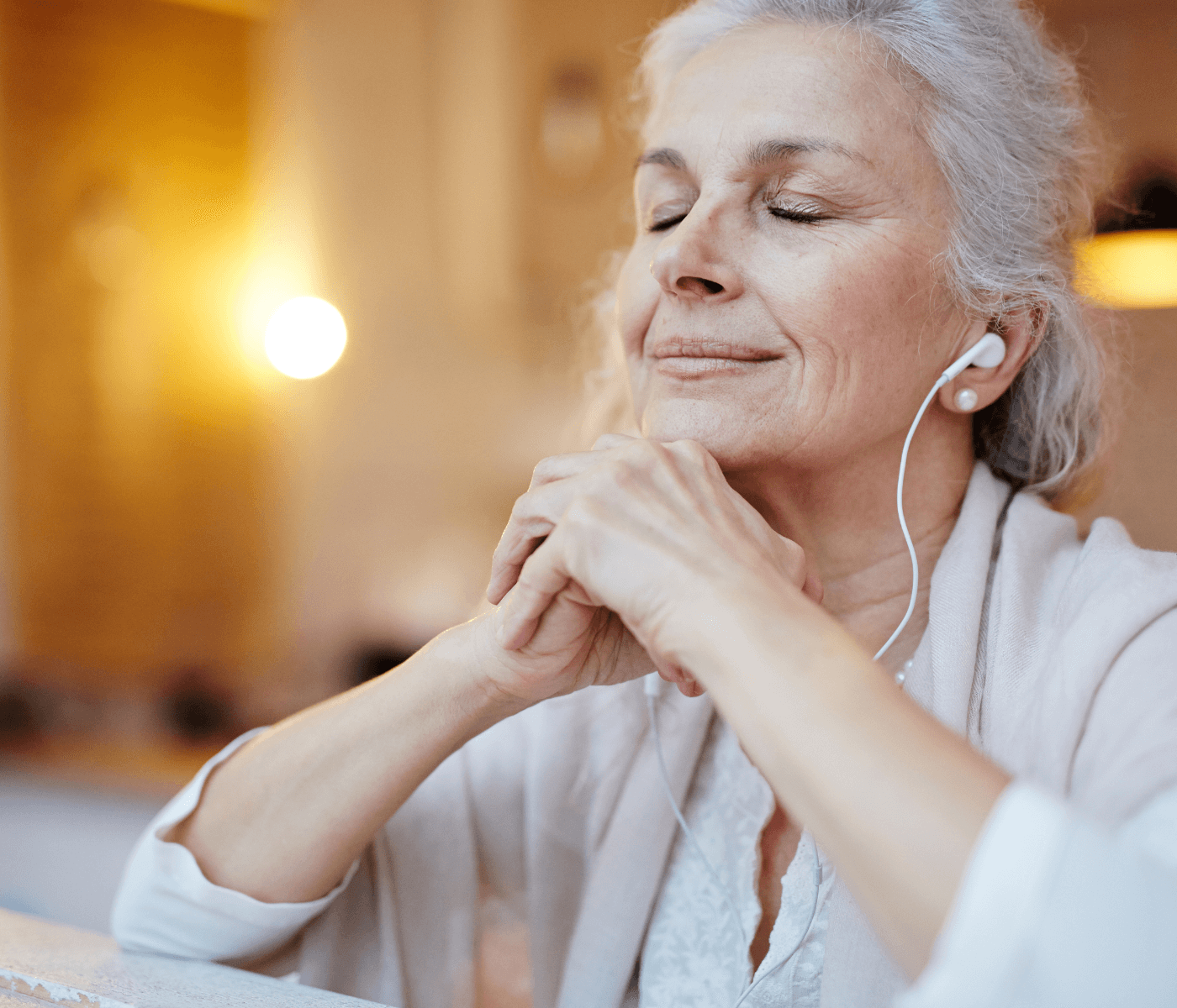 An elderly woman with headphones on, eyes closed, and hands clasped, enjoying a peaceful moment. - Home Instead