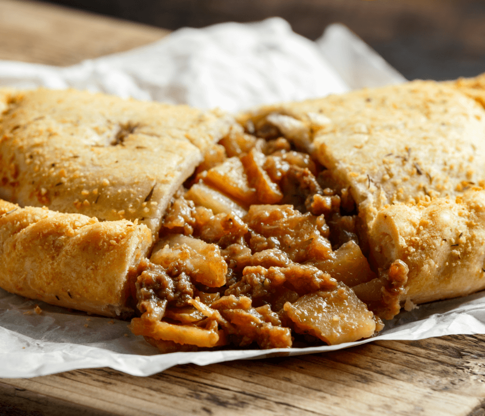 A savory pie cut open to reveal a filling of diced vegetables and meat on a rustic wooden surface. - Home Instead