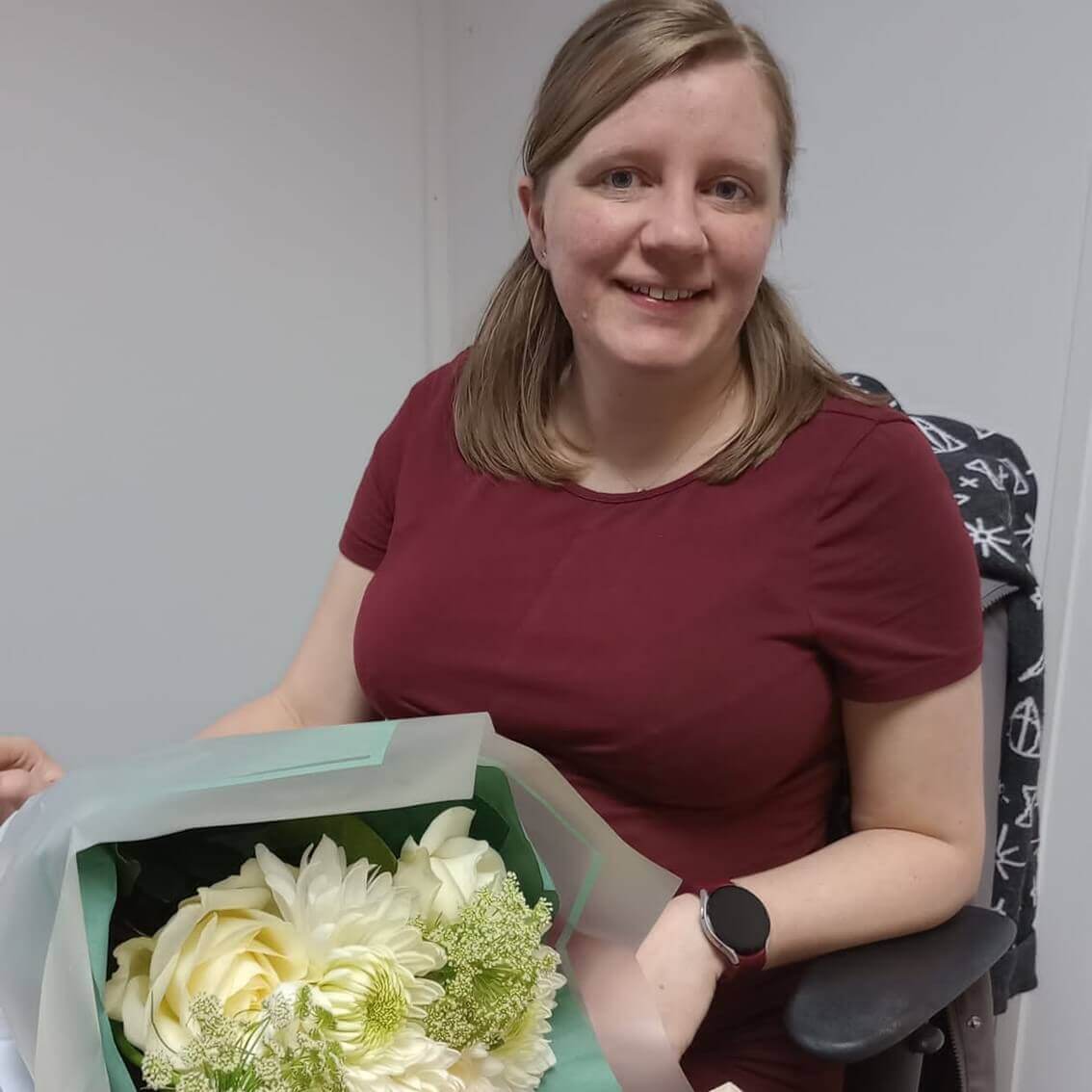 A woman smiles while holding a bouquet of white and green flowers wrapped in light green paper. - Home Instead