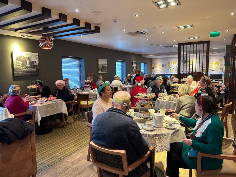 A group of elderly people wearing festive hats enjoy a meal together in a decorated restaurant. - Home Instead