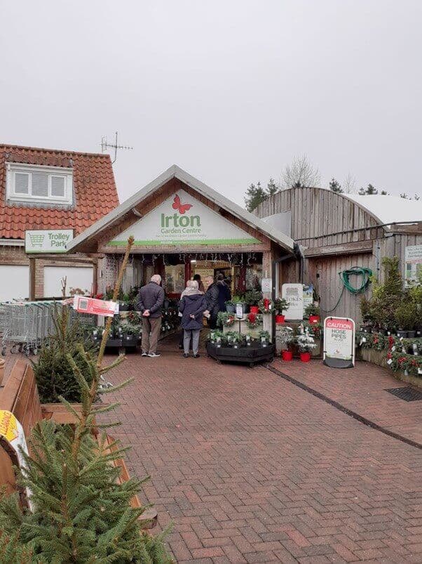 People standing at the entrance of Irton Garden Centre, with Christmas decorations and trees displayed outside. - Home Instead