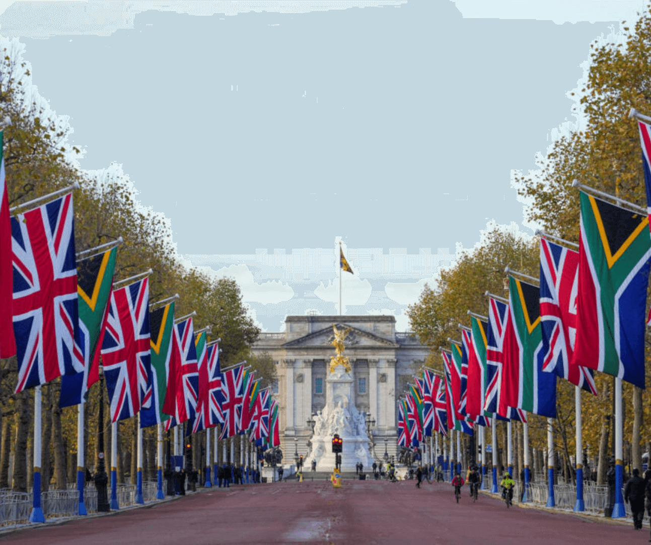Union Jacks and other flags line the road towards Buckingham Palace, with trees and pedestrians on both sides. - Home Instead
