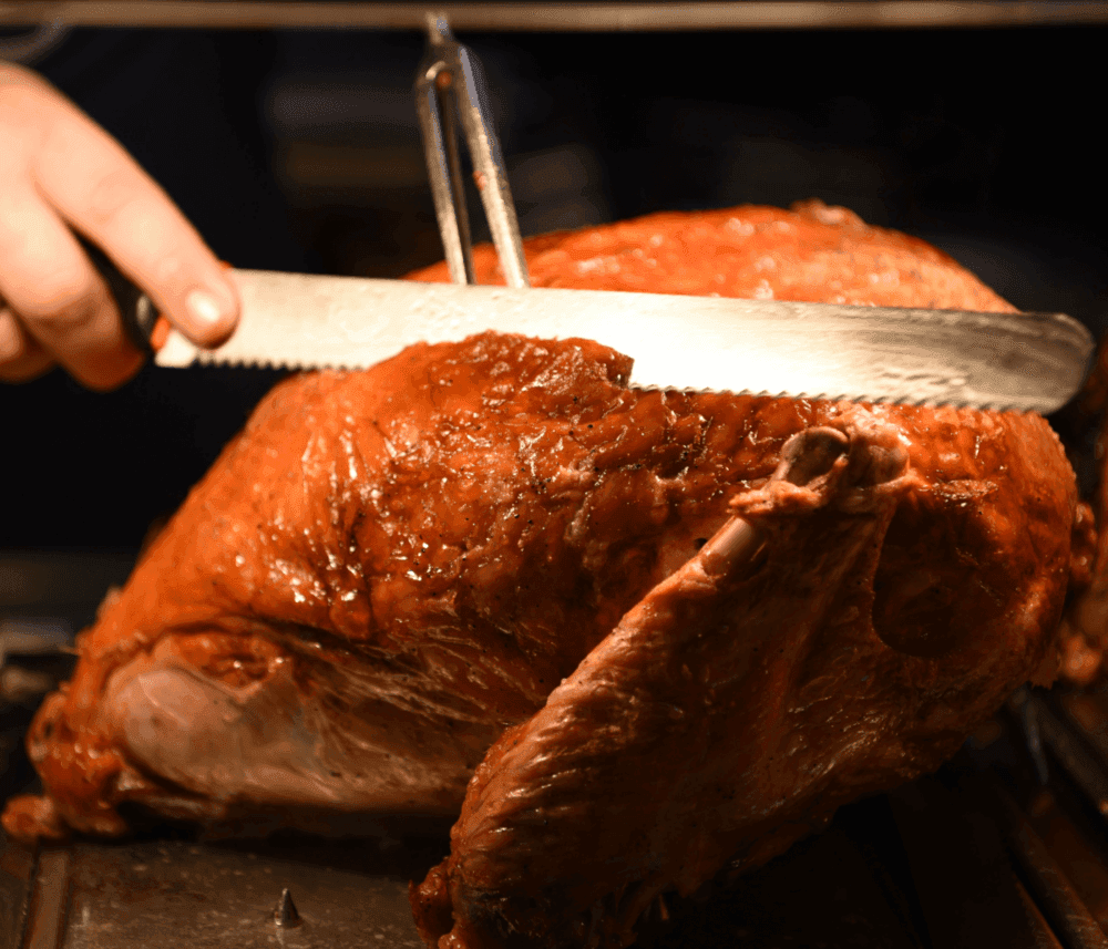Person carving a roasted turkey with a serrated knife. - Home Instead