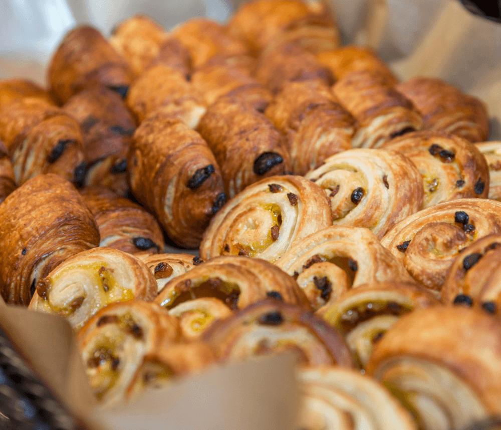 A variety of flaky pastries, including croissants and pain au chocolat, arranged on a tray. - Home Instead