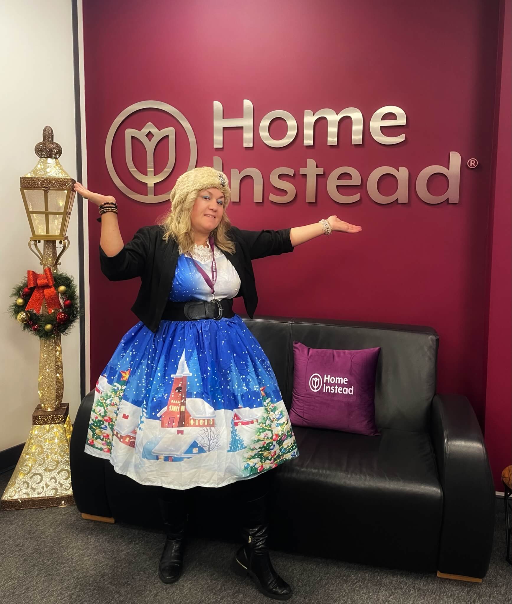 Person in a festive dress poses with arms raised in front of the "Home Instead" sign and a decorative lamp post. - Home Instead