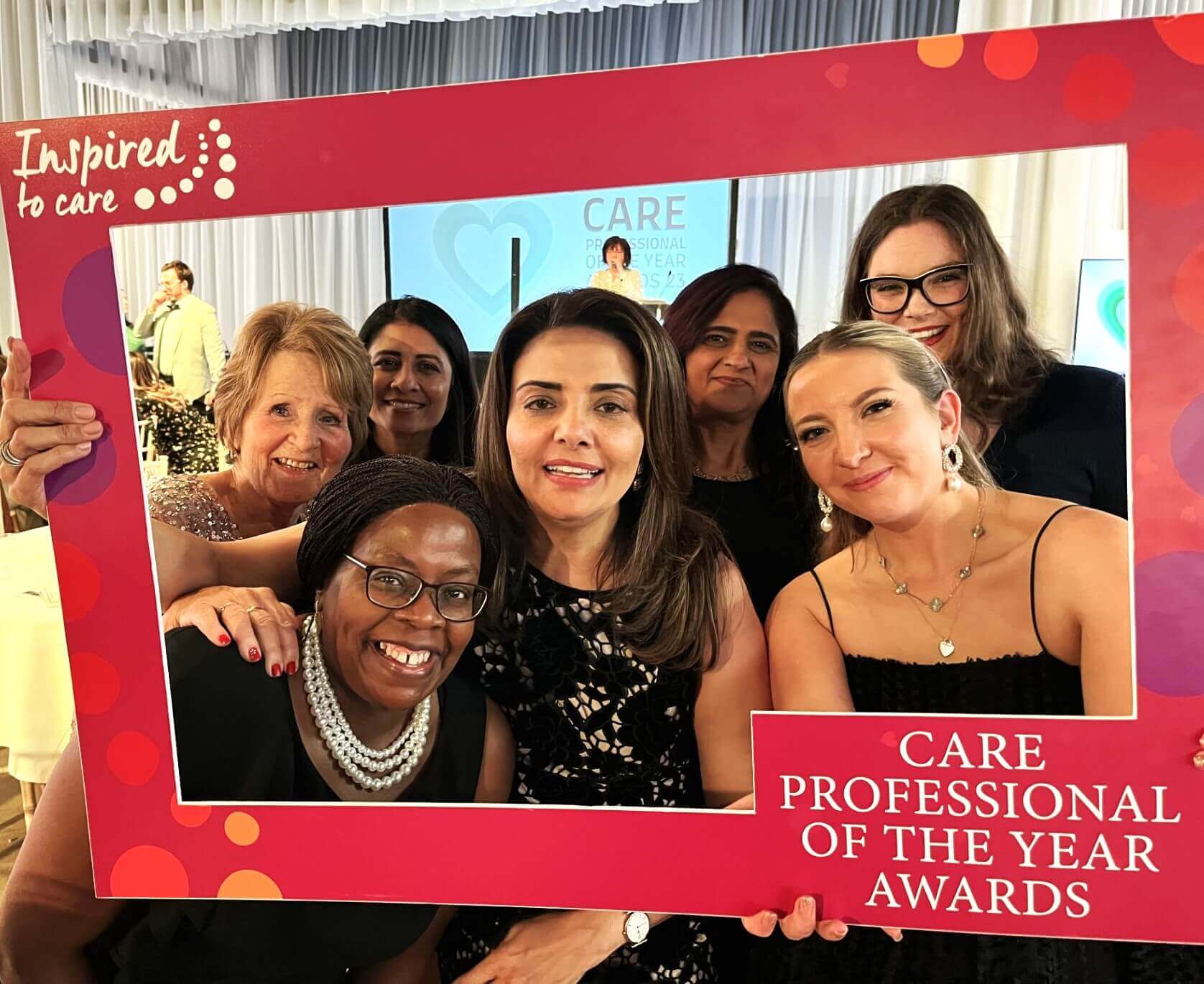 A group of people smiling and posing with a "Care Professional of the Year Awards" frame at an event. - Home Instead