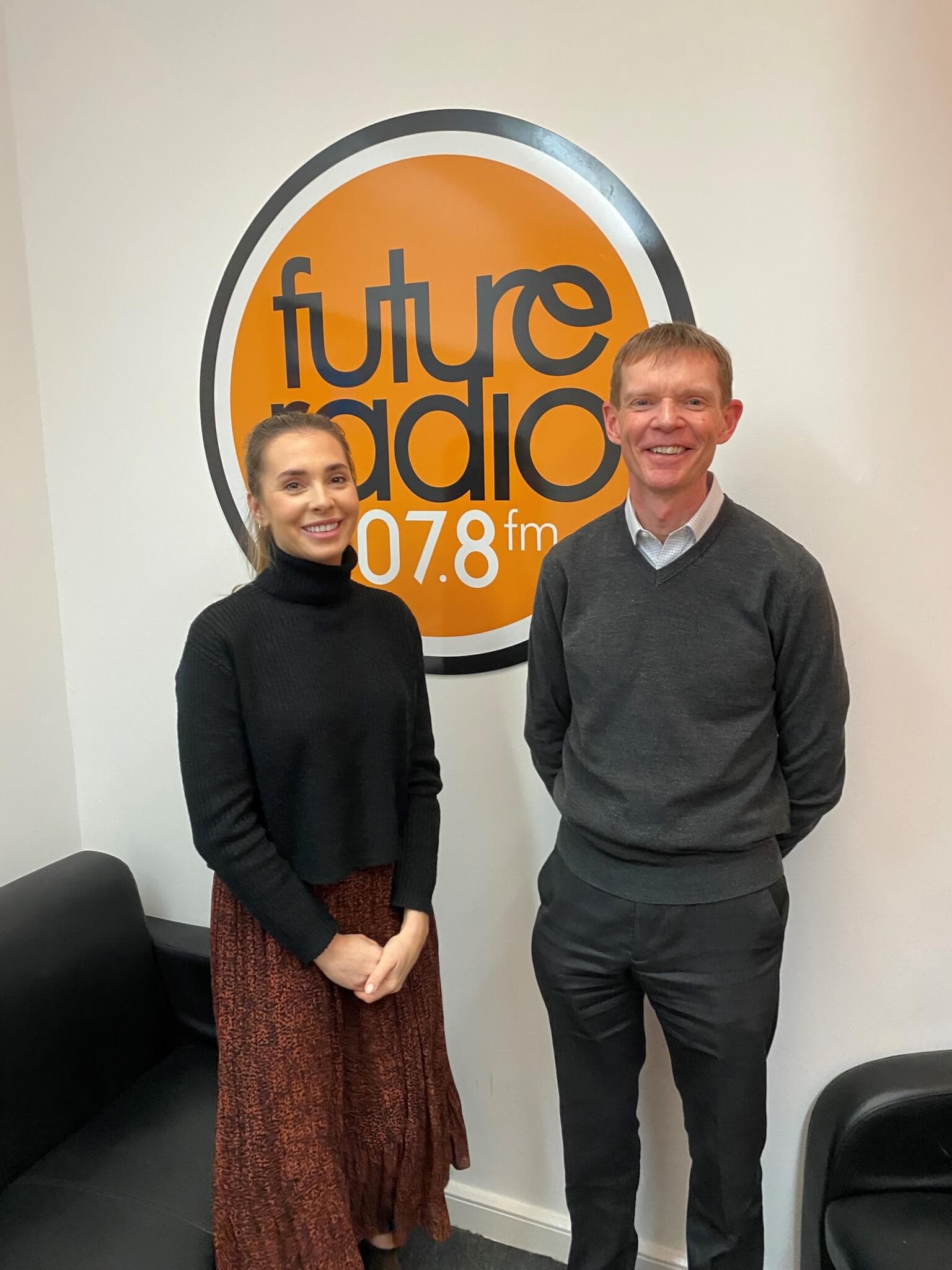 Two people standing in a radio station studio in front of a "future radio 107.8 fm" logo on the wall. - Home Instead