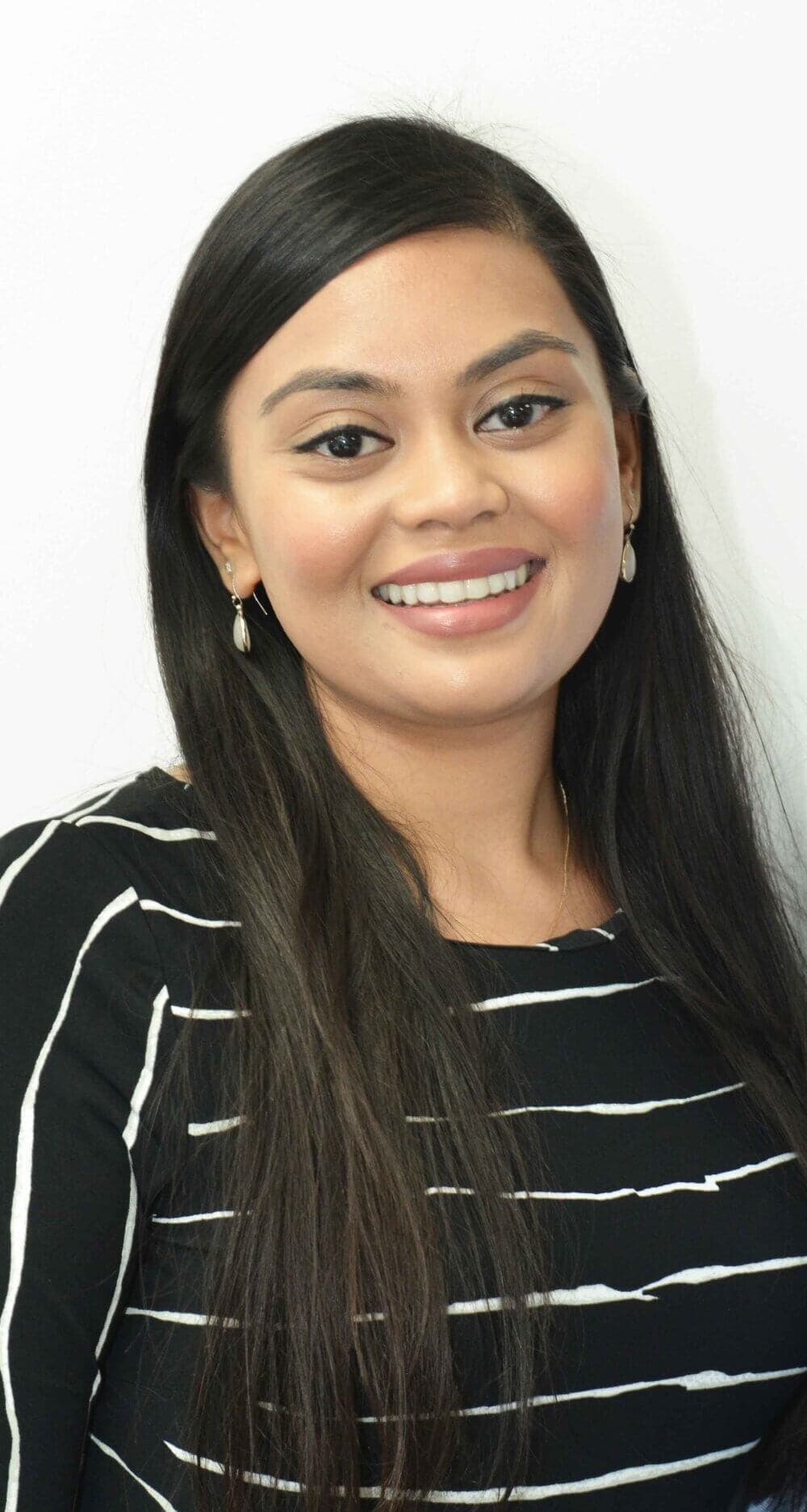 A woman with long dark hair, wearing a black and white striped top, smiles against a plain white background. - Home Instead