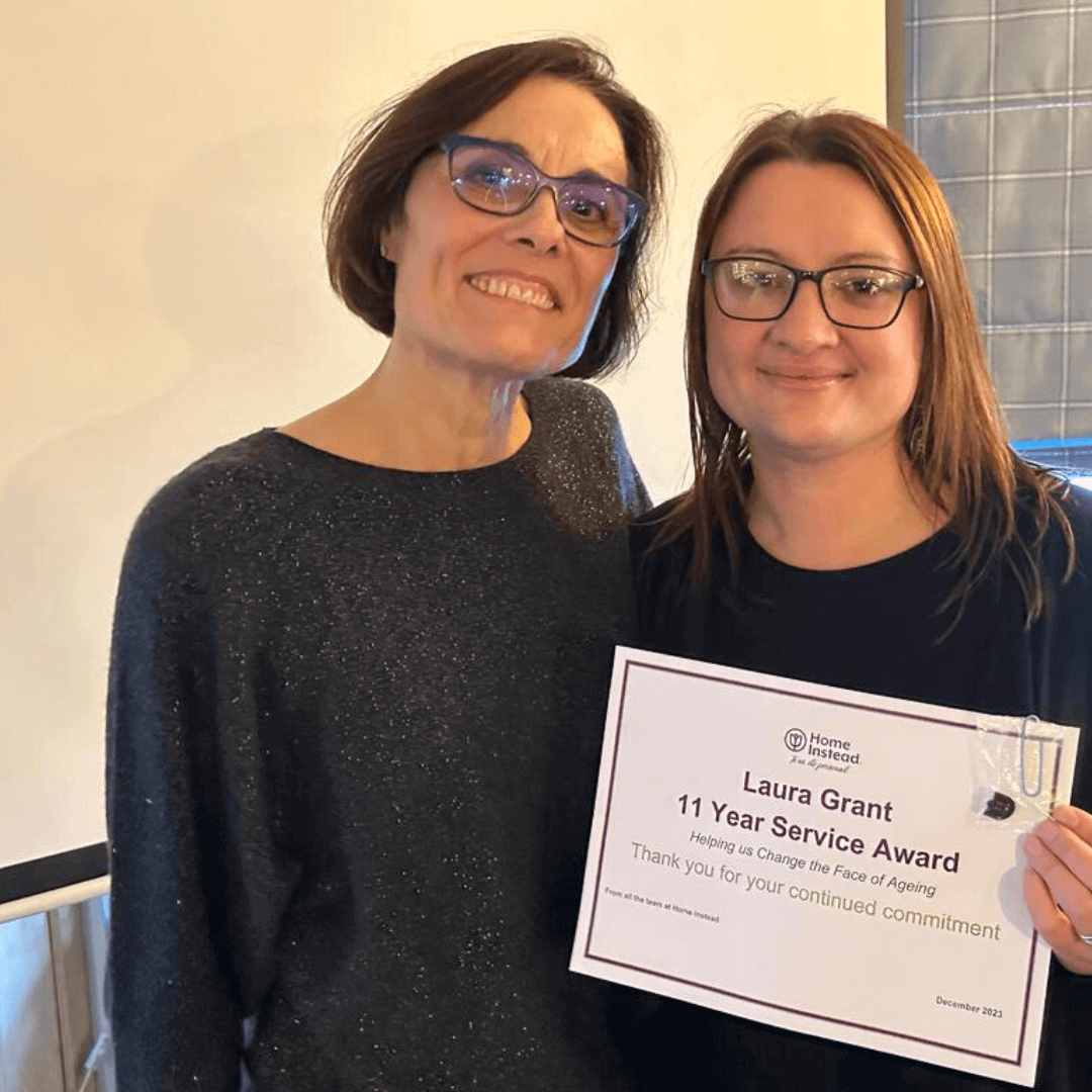 Two women smiling, holding a certificate for Laura Grant's 11 Year Service Award. - Home Instead