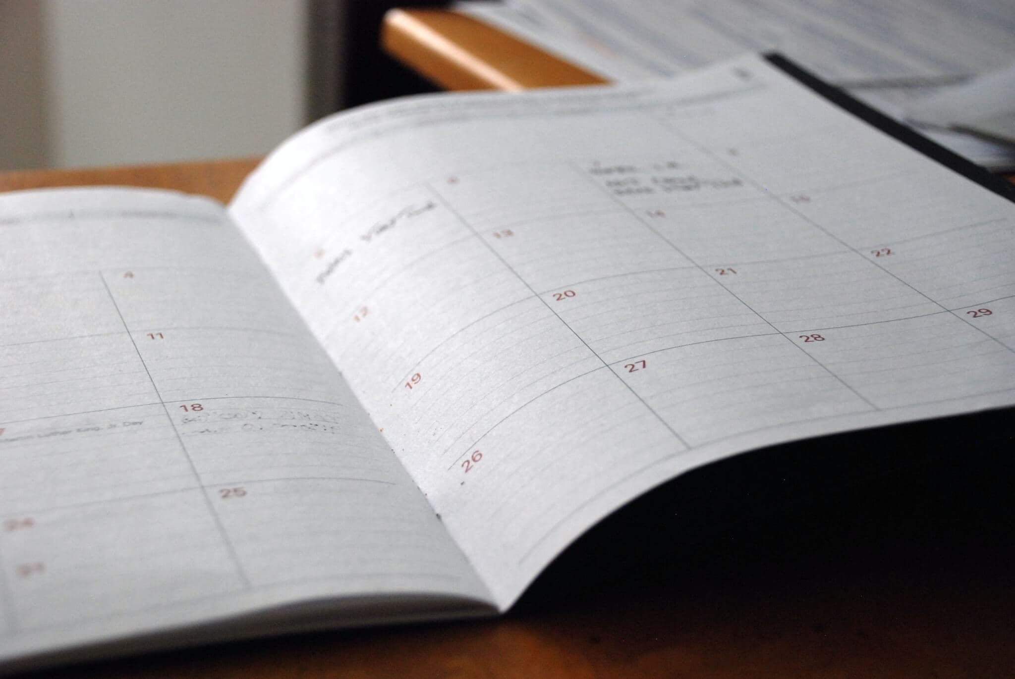 Open planner on a wooden desk, showing a monthly calendar with handwritten notes on some of the dates. - Home Instead