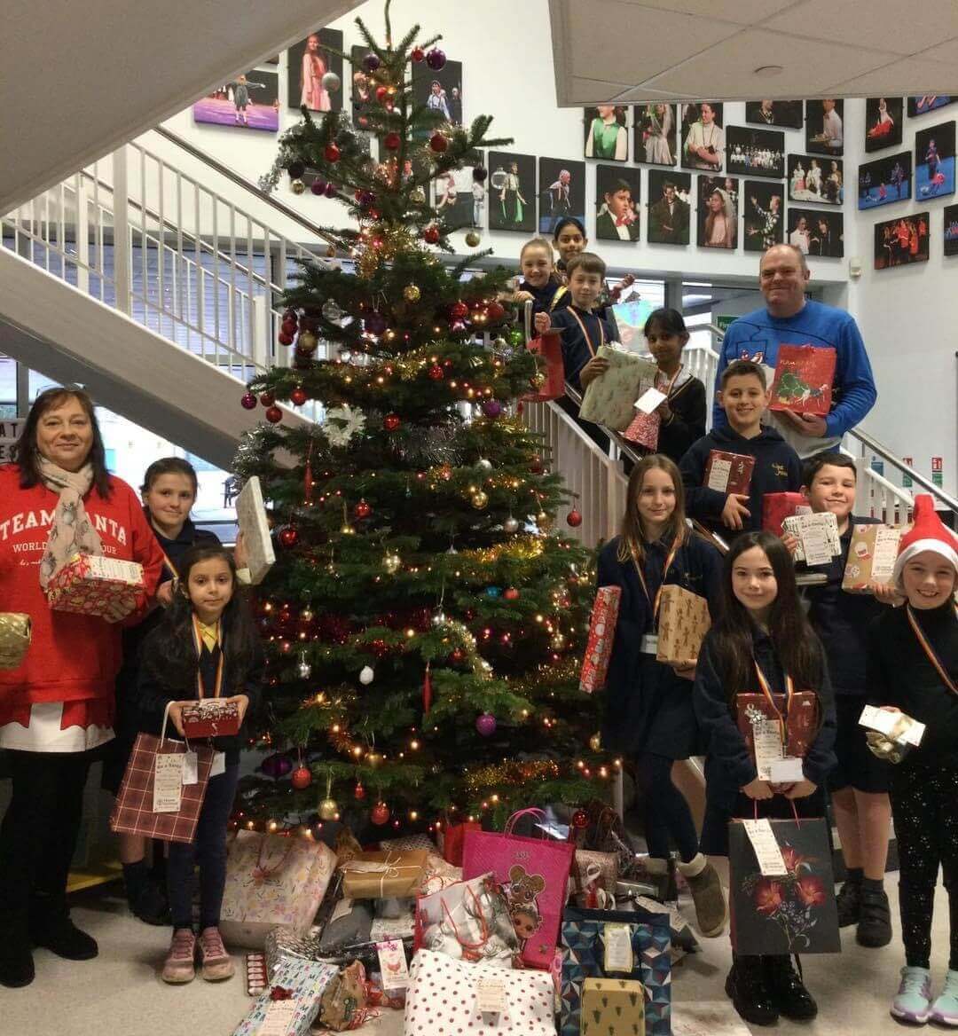 Group of people of diverse ages holding gifts and standing by a decorated Christmas tree inside a building. - Home Instead