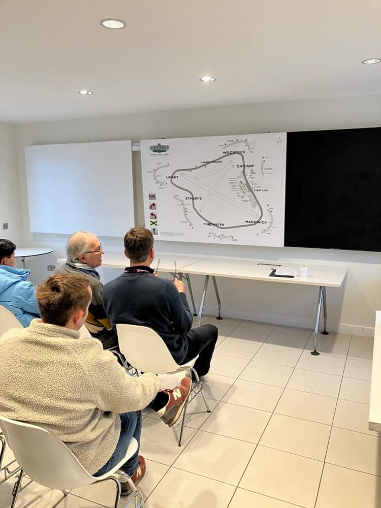 People seated in a room facing a large map posted on the wall, engaged in discussion. - Home Instead