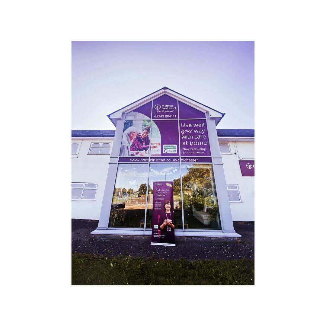 Exterior of a building with large windows displaying Home Instead signage and a banner promoting elderly care services. - Home Instead