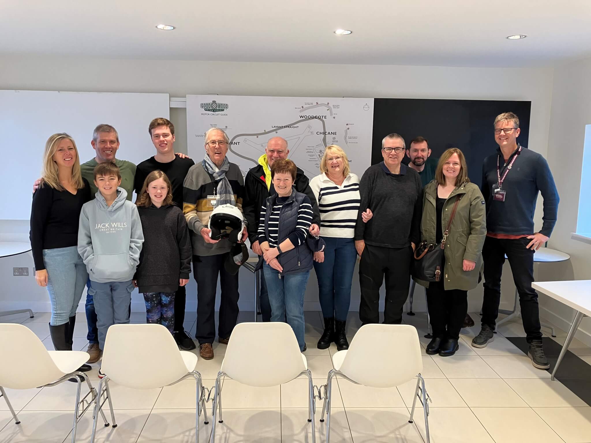 A group of people posing together in a bright room with white chairs and a wall map in the background. - Home Instead