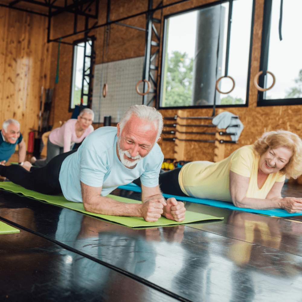 A group of elderly individuals smiling while doing plank exercises on yoga mats in a modern fitness studio. - Home Instead
