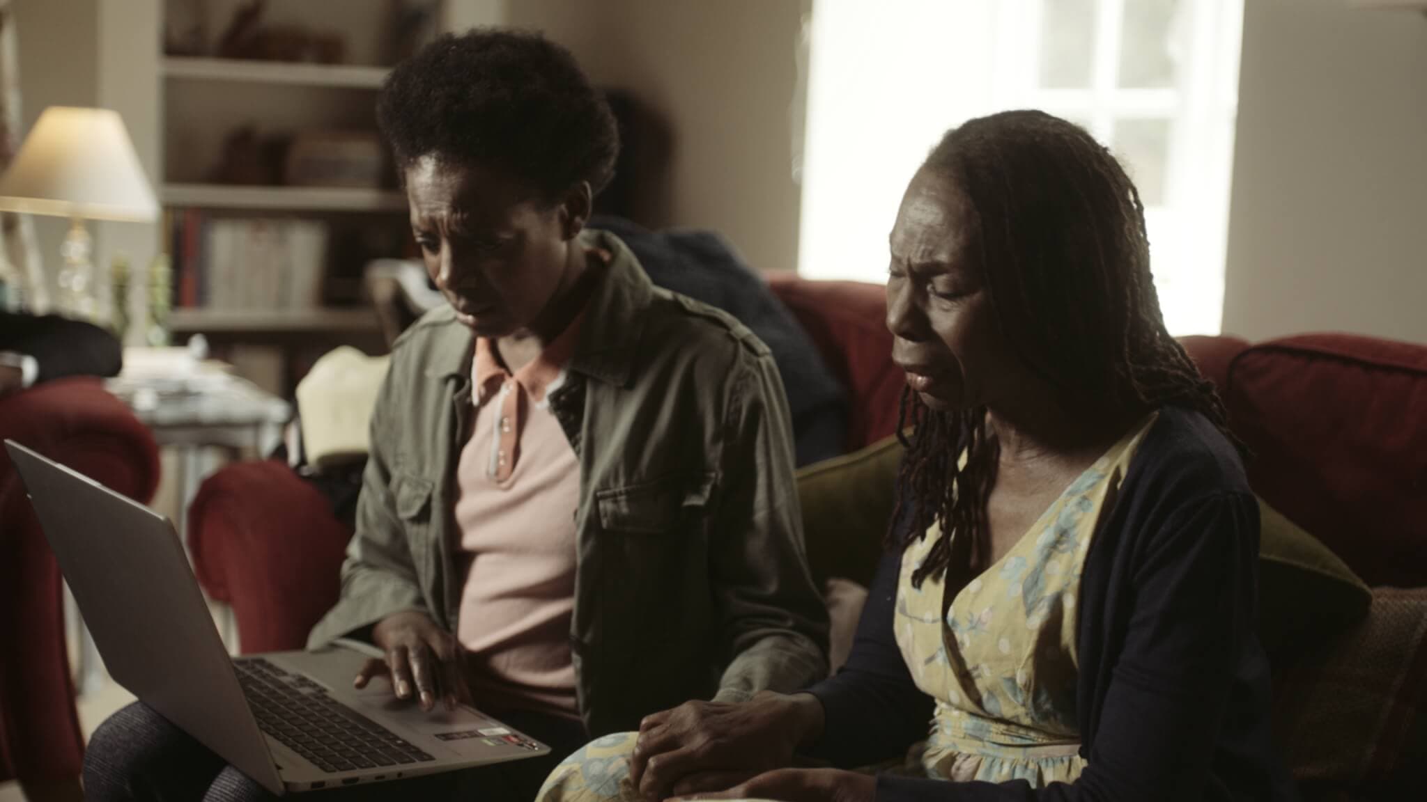 Two people sitting on a couch, looking at a laptop with concerned expressions in a living room setting. - Home Instead