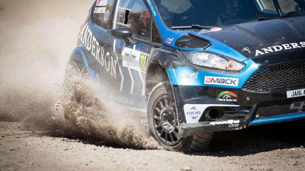 A rally car skids on a dirt road, kicking up dust during a race. - Home Instead