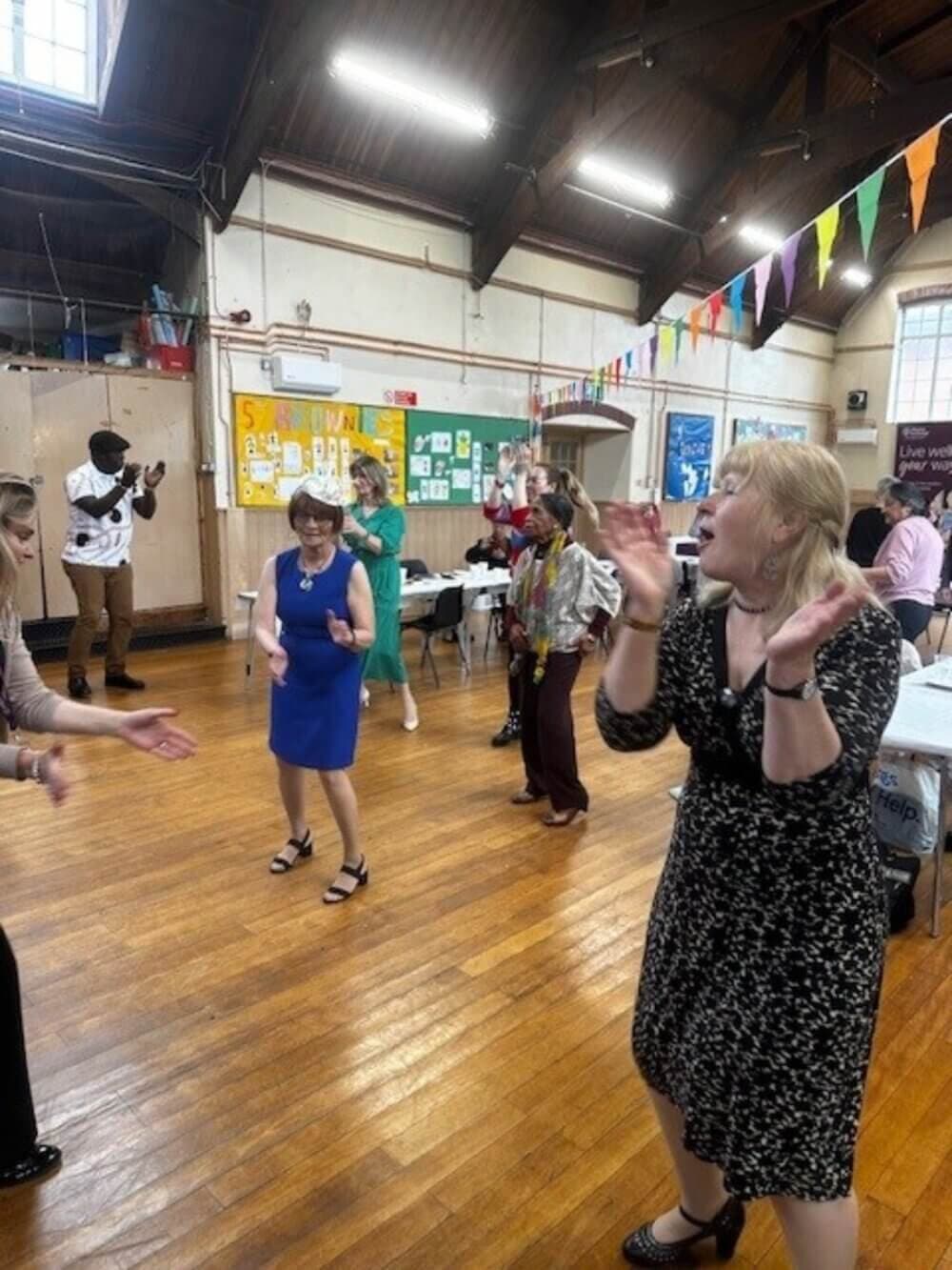 A group of people dancing and clapping in a festive, indoor space decorated with colorful flags. - Home Instead