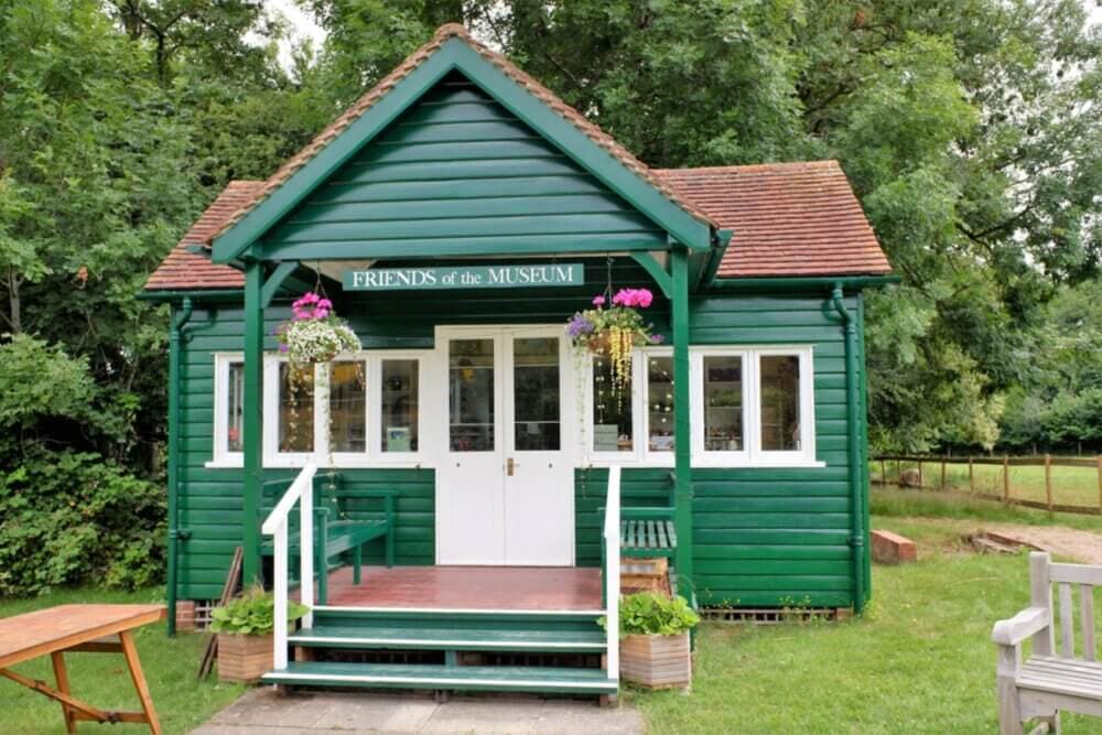A small green building with a sign reading "Friends of the Museum," surrounded by greenery and flowers hanging outside. - Home Instead