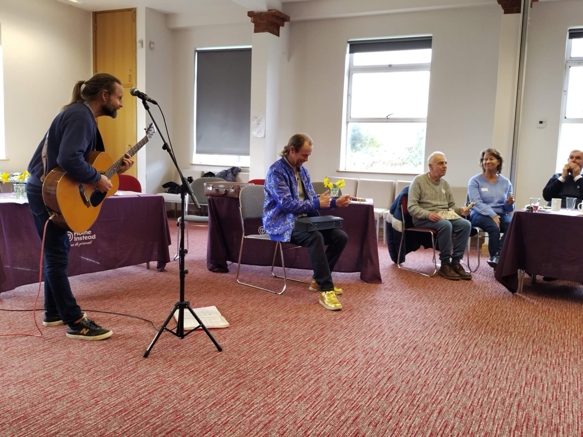 Person playing guitar at Home Instead event while elderly people enjoy the music