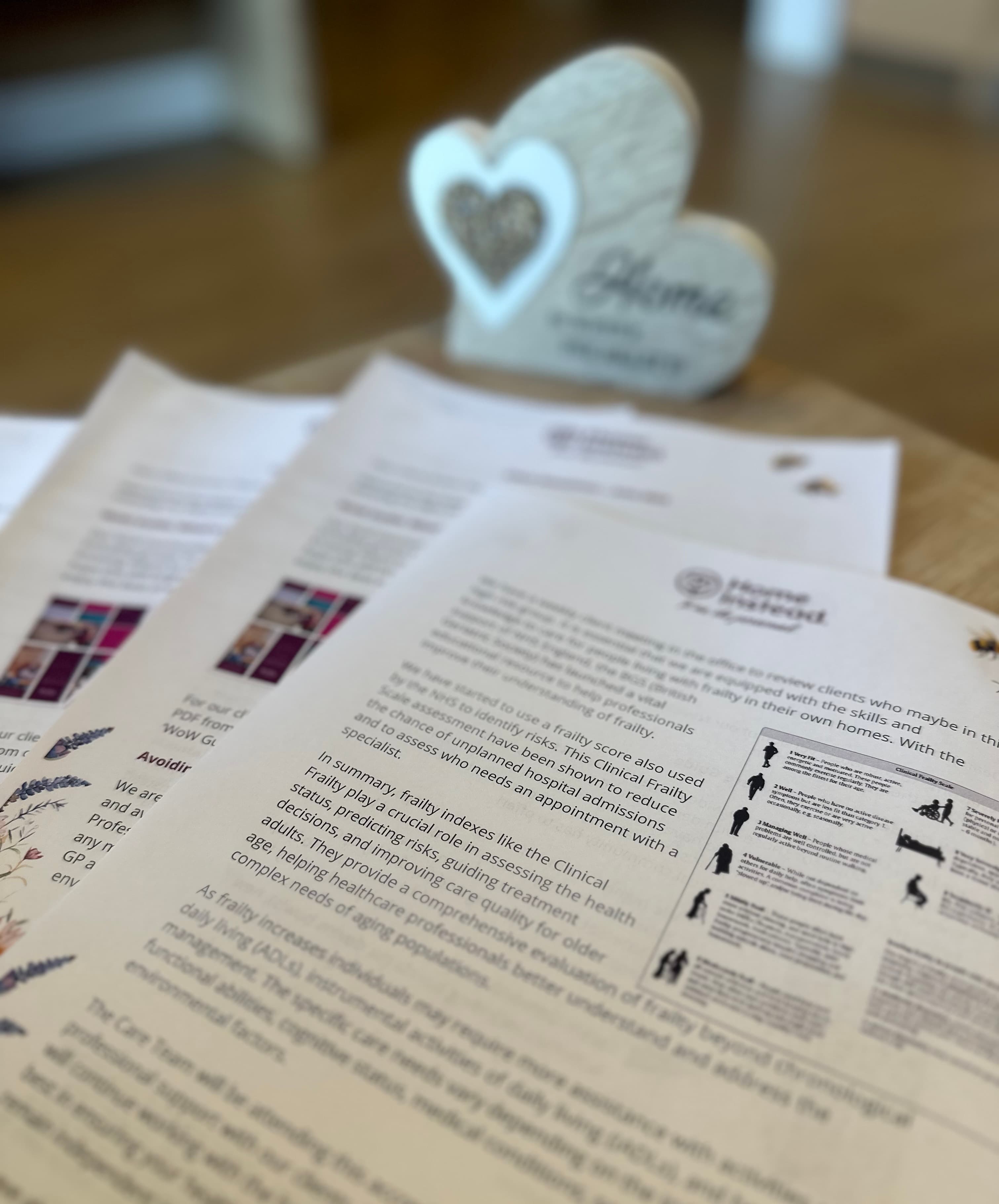 Close-up of printed documents on a surface, with a blurred heart-shaped ornament in the background. - Home Instead