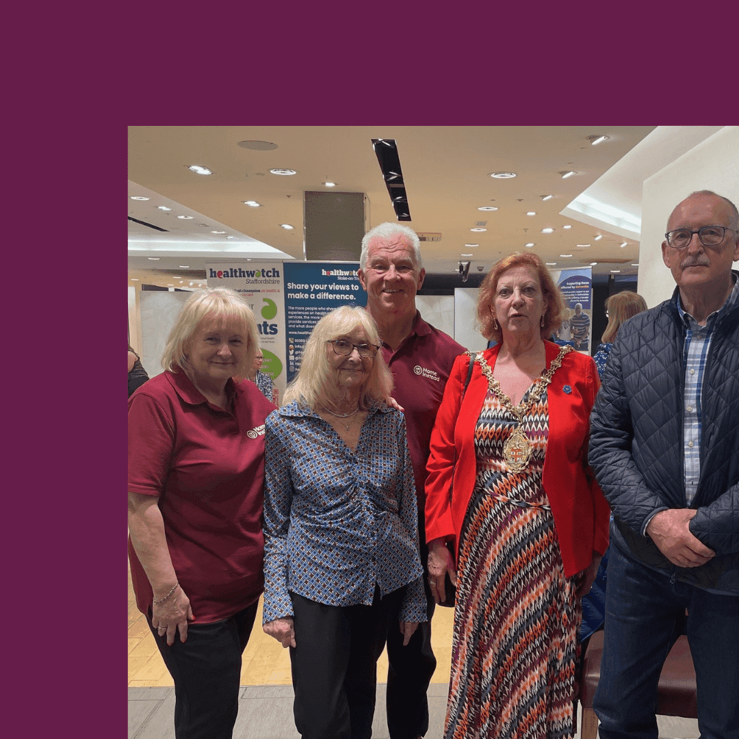 A group of five people standing together at an event, smiling for the camera. Booths and banners are visible behind them. - Home Instead
