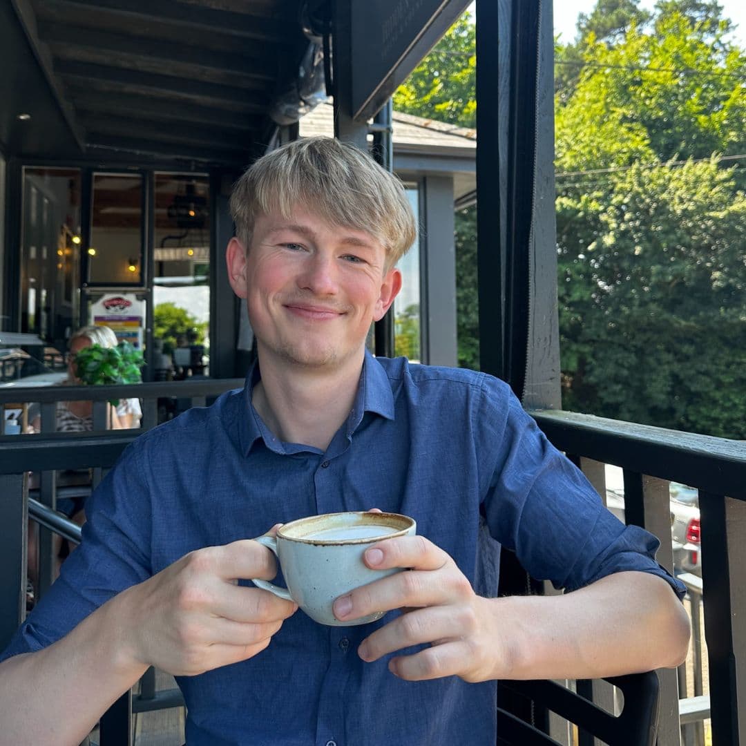 Adam smiling, holding a coffee