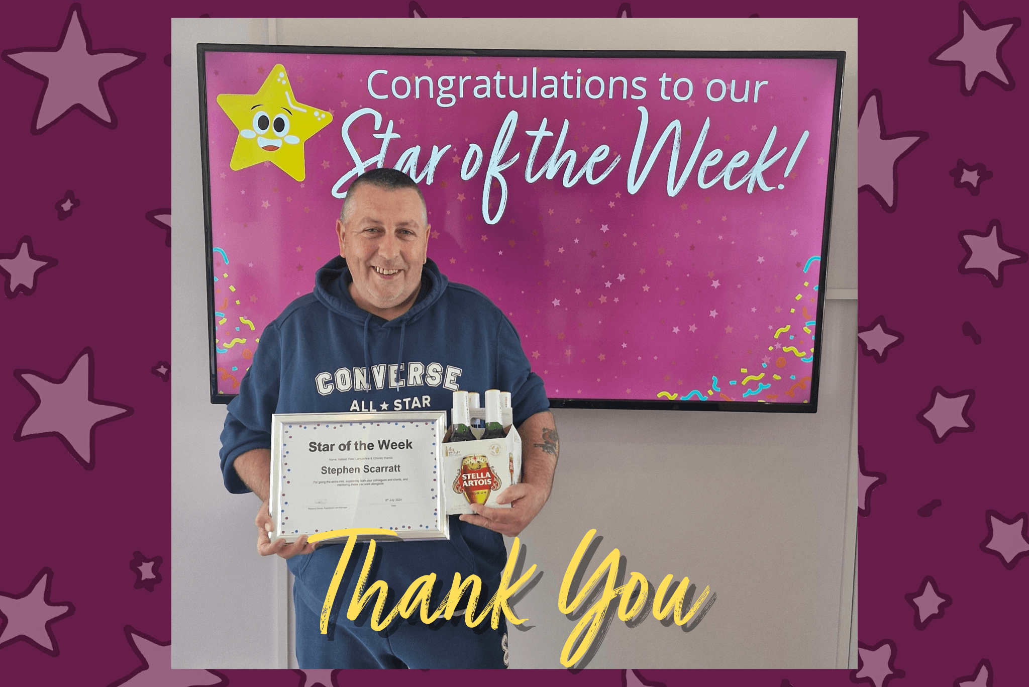 Man holding "Star of the Week" certificate and gift basket, standing in front of "Star of the Week" congratulatory sign. - Home Instead