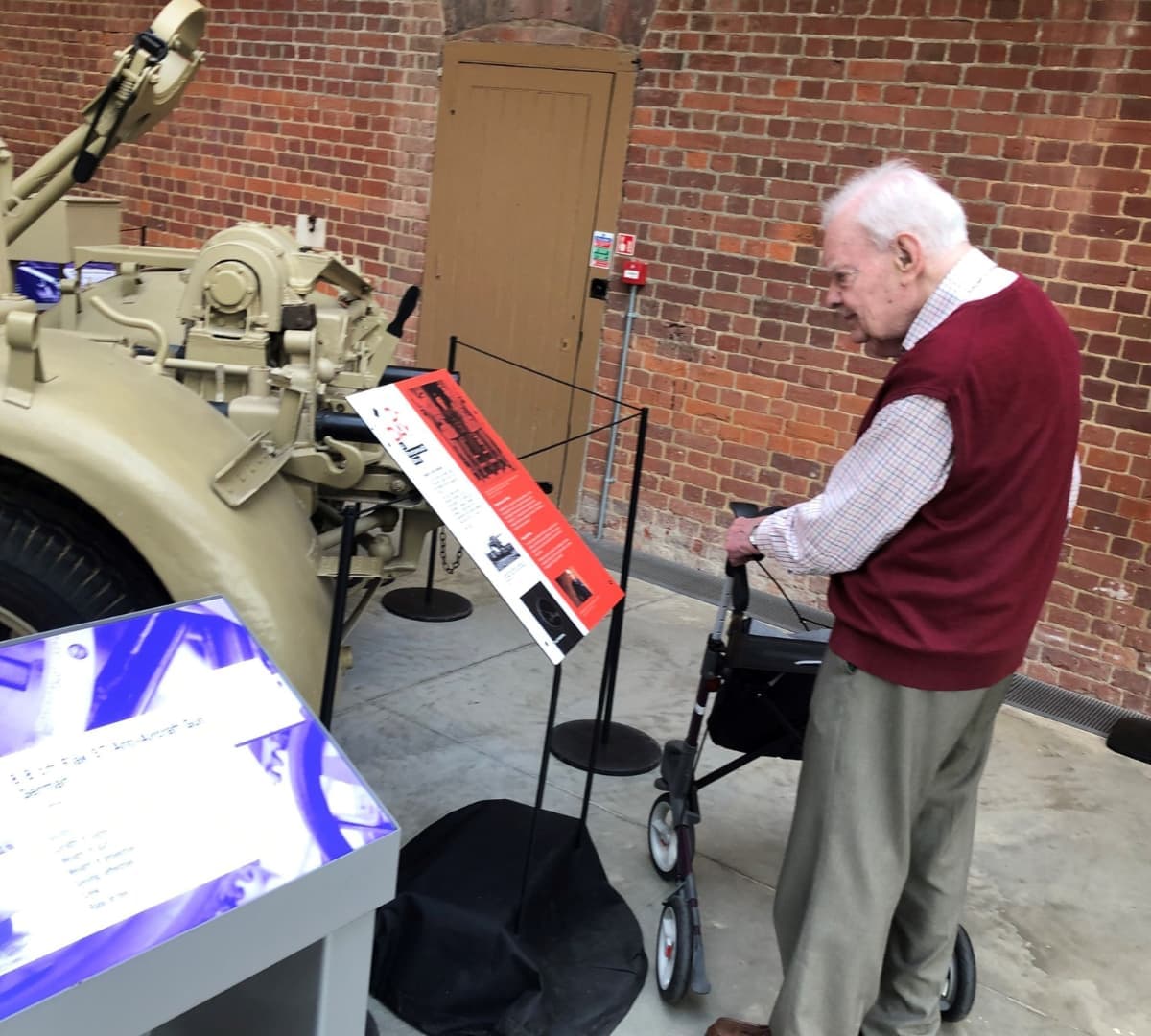 Old man standing while using a walker and looking inside a room and reading an information