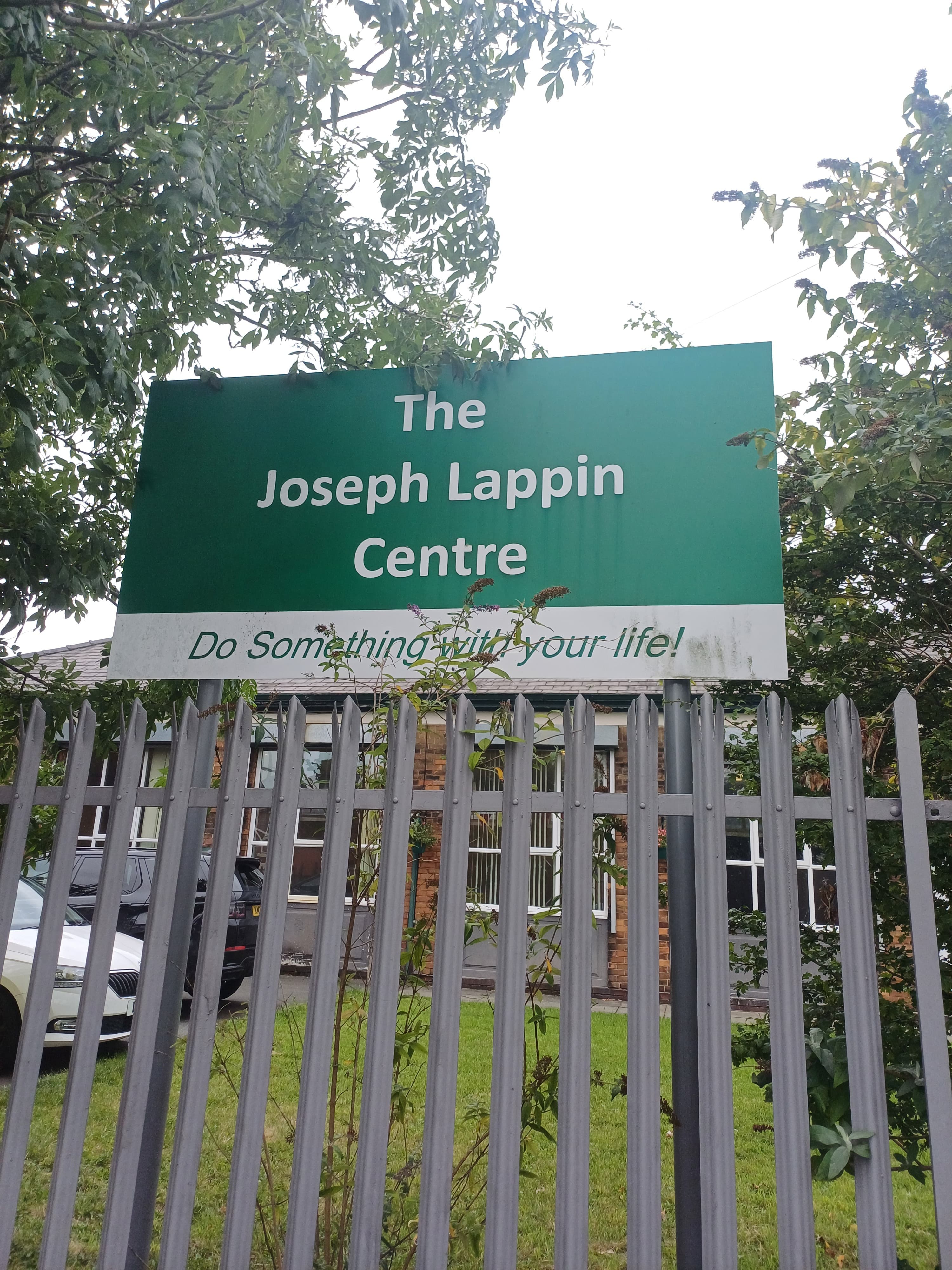 Sign reading "The Joseph Lappin Centre" with the motto "Do Something with your life!" behind a fence with trees around. - Home Instead