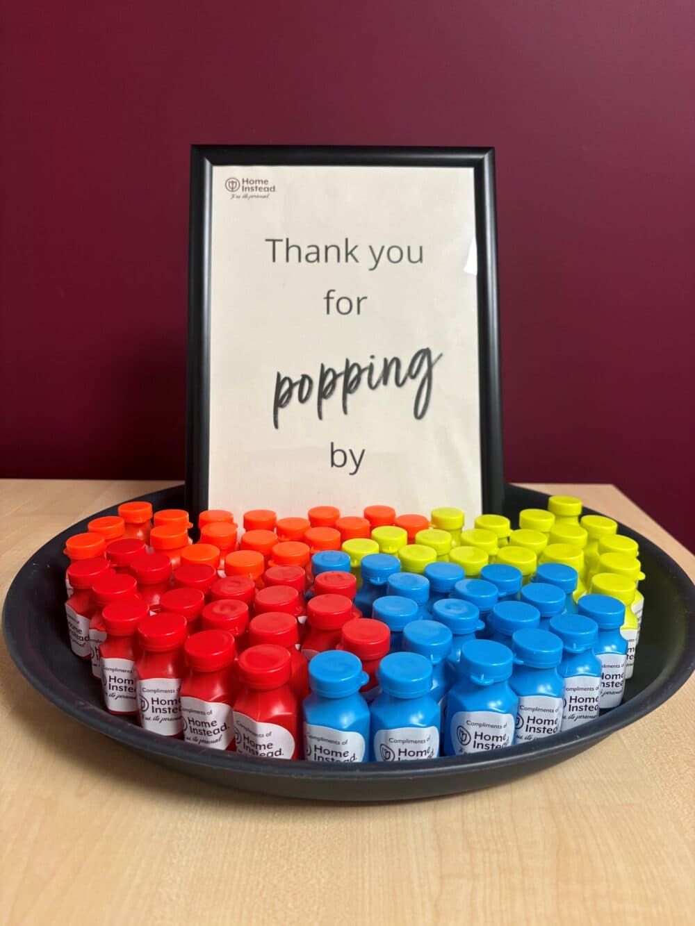 Tray of colorful mini bubble bottles in front of a sign that reads "Thank you for popping by. - Home Instead