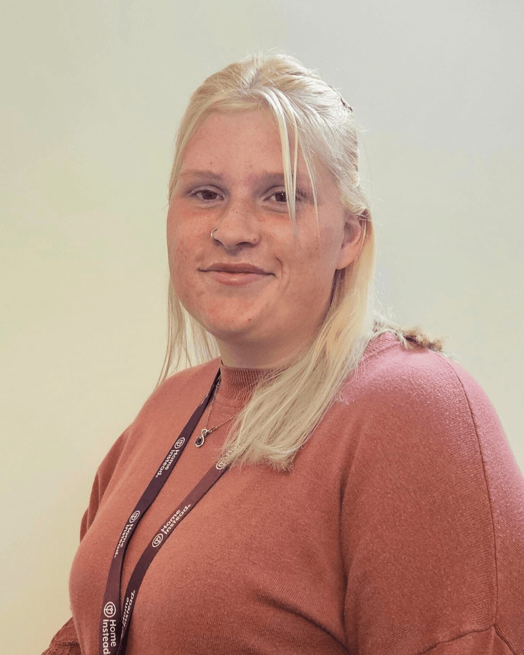 A woman stands next to a Home Instead sign in a library setting with brochures and a laptop on the table. - Home Instead