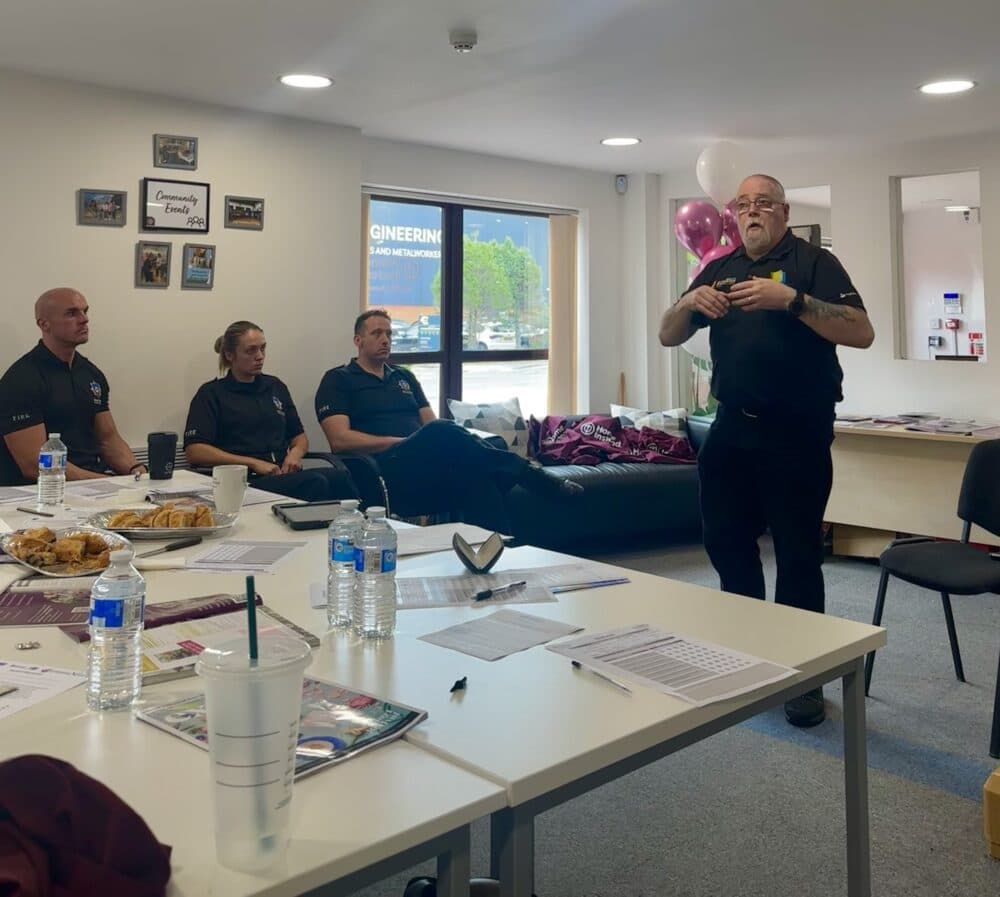 A man gives a presentation to four seated people in an office with tables and chairs. - Home Instead