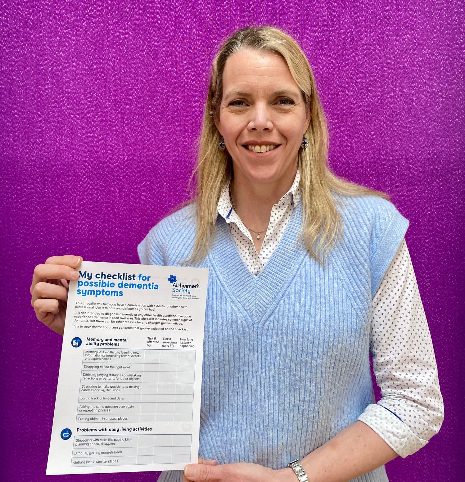 Person holding a dementia symptoms checklist against a purple background, smiling. - Home Instead