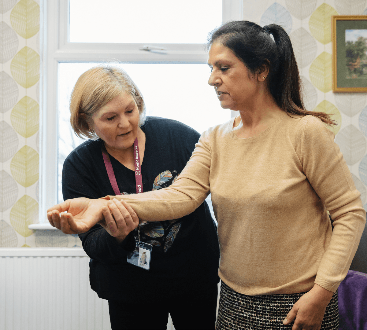 A woman wearing black with ID teaching another woman by holding her arms who is wearing beige with black long hair inside a room