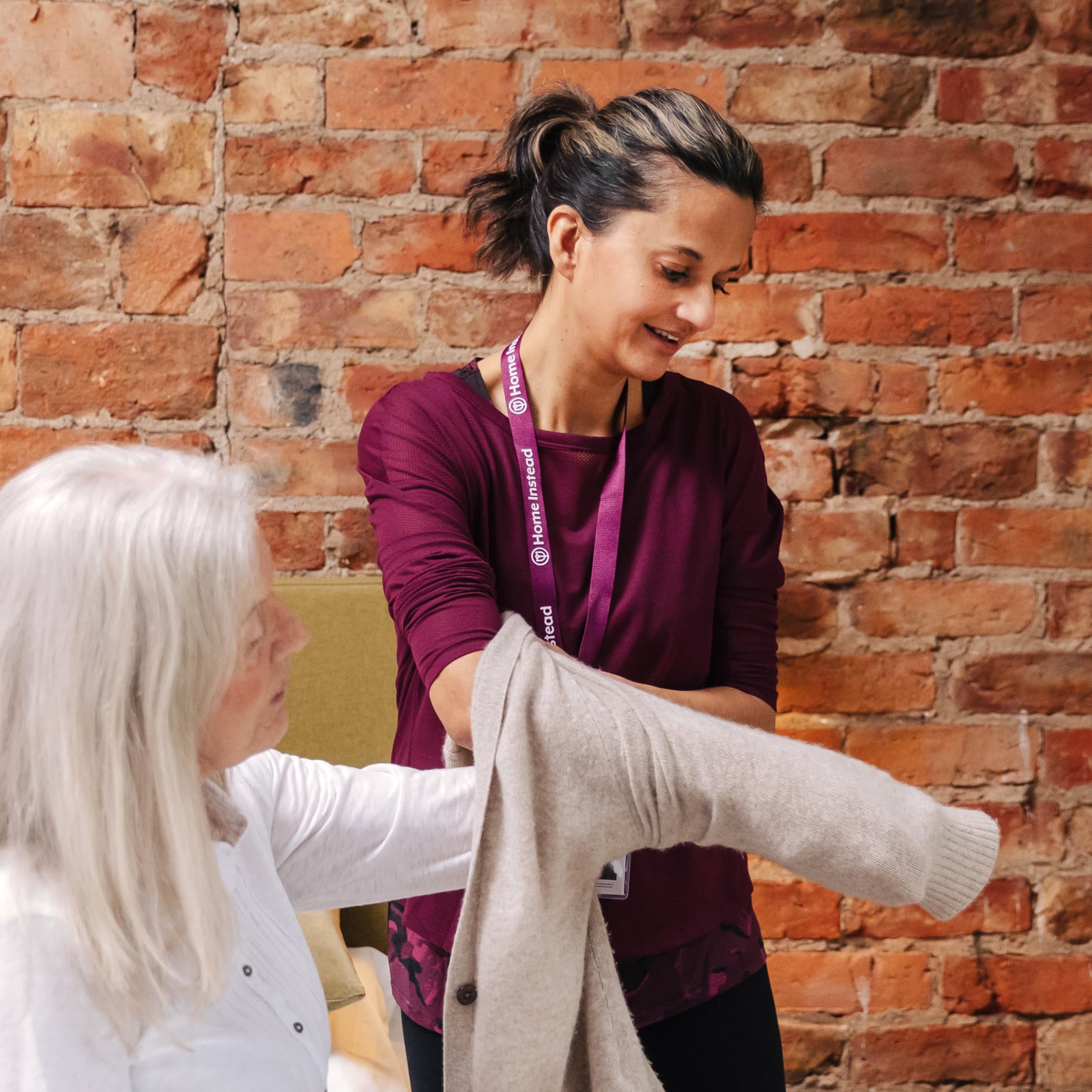 Female care professional on personal care visit helping client get dressed