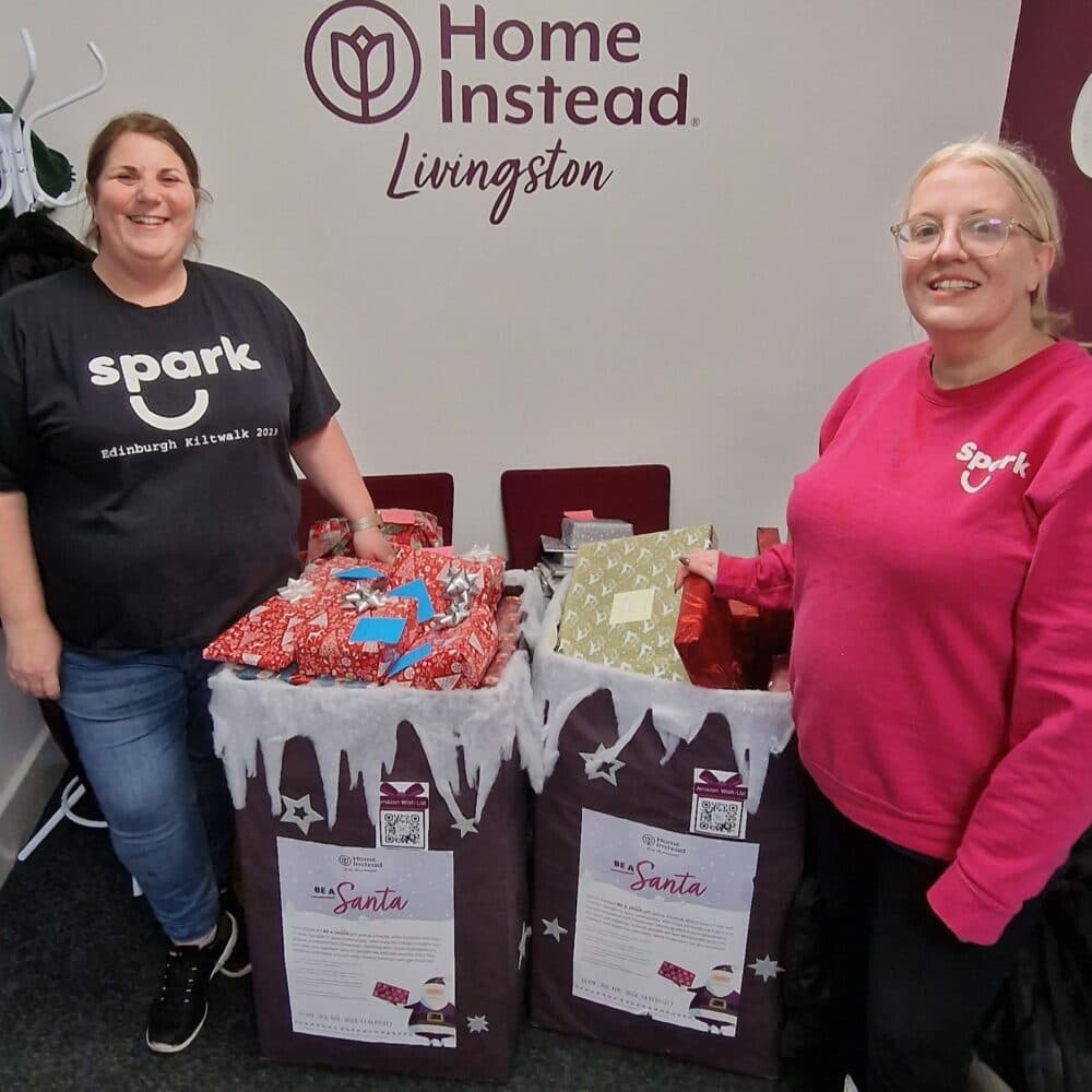 Two people standing next to collection bins full of Christmas presents - Home Instead