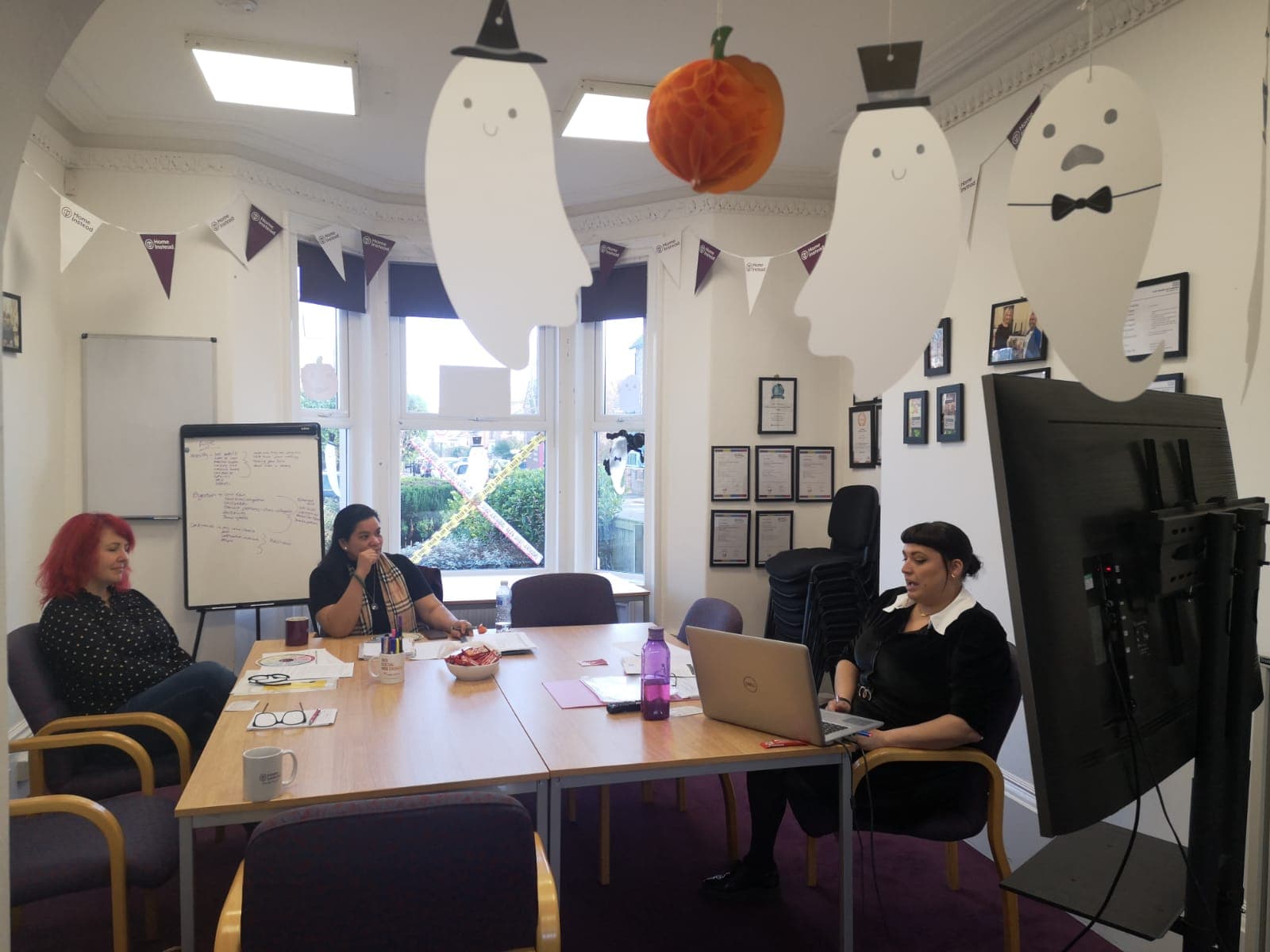 Halloween Training at the Home Instead Newcastle Office, with two care pro's sat at the table, and the trainer at the other side with a laptop delivering training. Halloween decorations are hung up on the ceiling.
