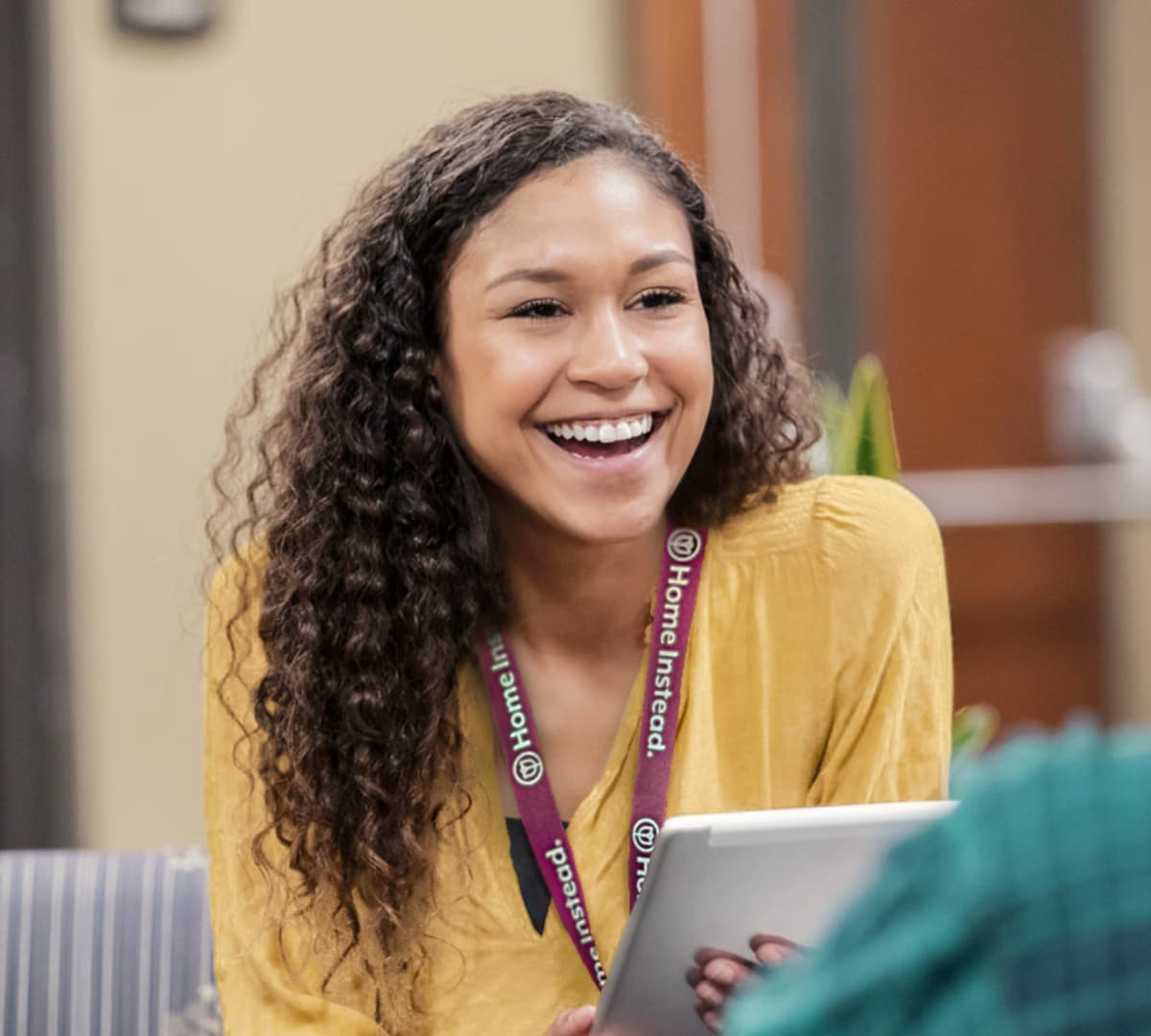 A lady smiling with curly hair and wearing a yellow shirt while holding a book