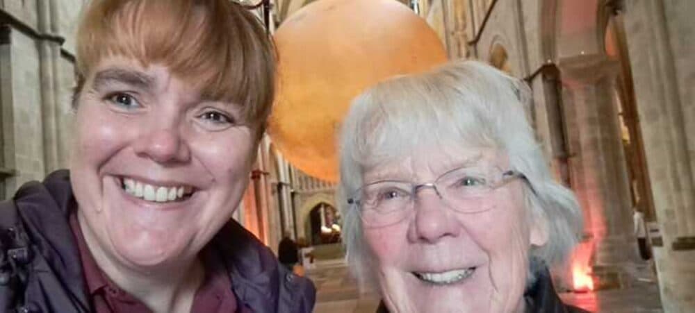 Two smiling women pose inside a cathedral with a large globe installation in the background. - Home Instead