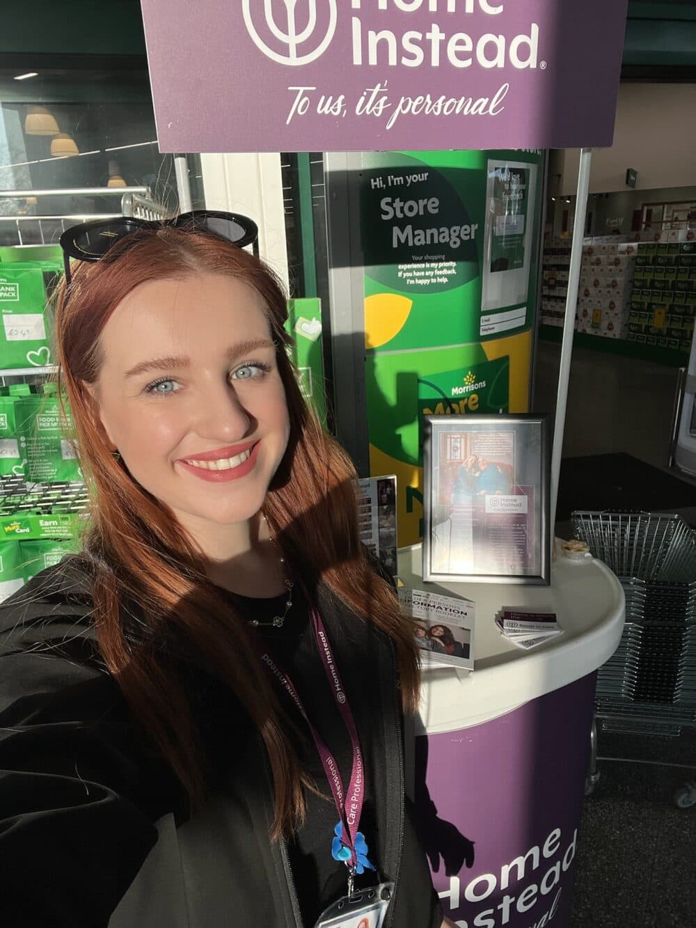 Smiling woman takes a selfie at a Home Instead booth inside a store, sunlight shining on her face. - Home Instead