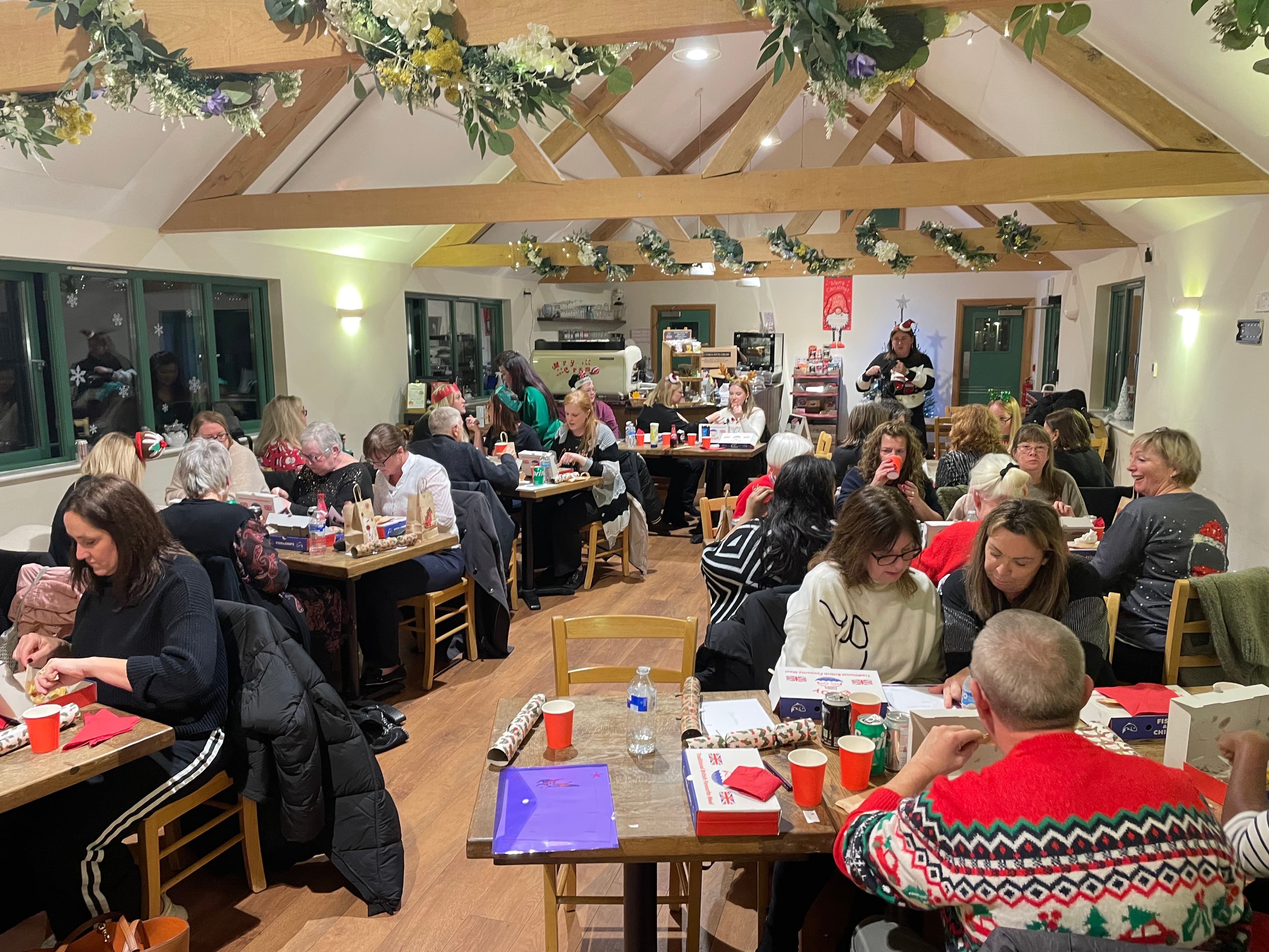 People sitting at tables in a festive, decorated room, wrapping gifts and socializing. - Home Instead