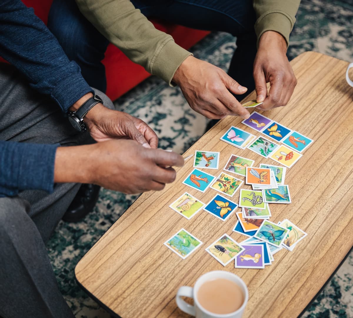 Two pair of hands with a memory game on a brown table and a cup of coffee