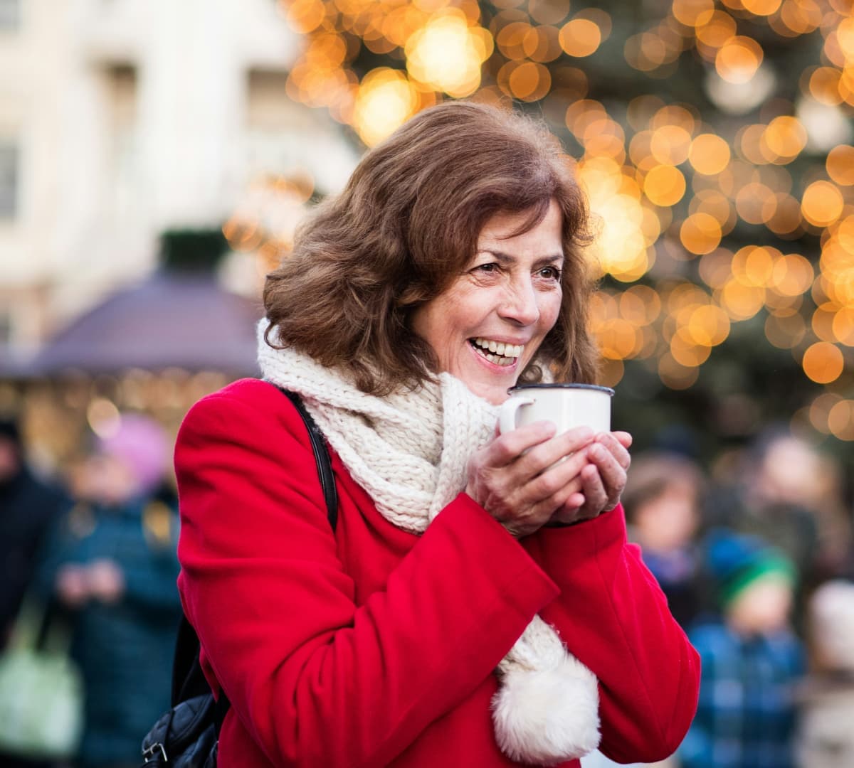 Older adult drinking coffee outdoors while wearing red winter clothes and smiling