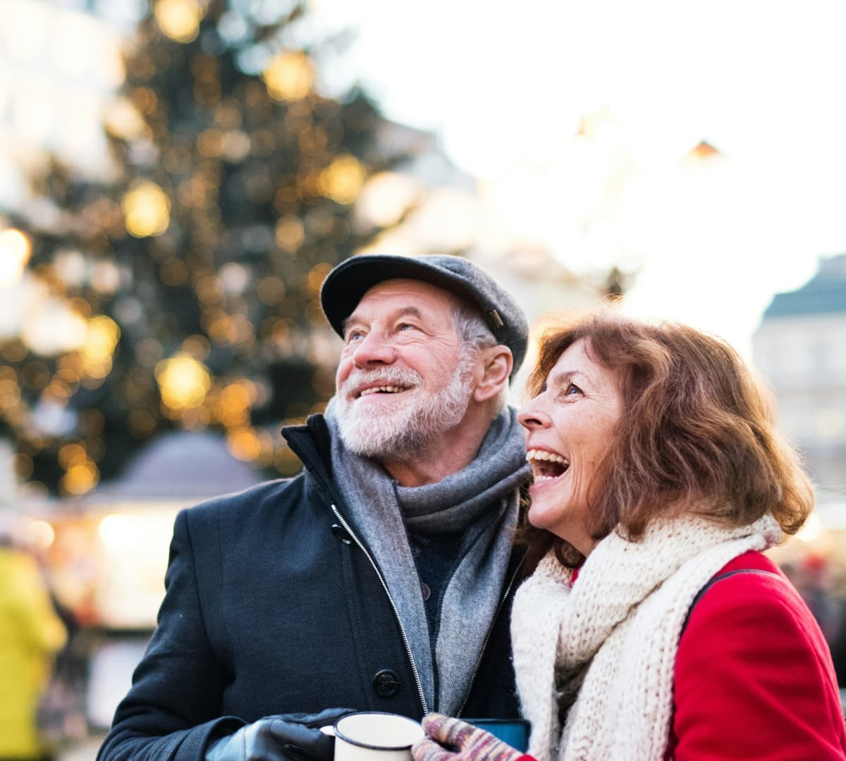 Two older adults, a male and female outdoor at winter time both wearing winter clothes and smiling and happy while looking at a view