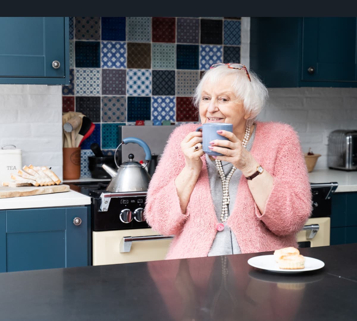 Woman with white hair and happy and smiling while sipping a cup of tea in the kitchen